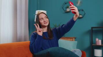 Woman on sofa at home with smartphone taking selfie on mobile phone cam, virtual call online video