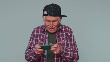 Worried funny addicted elderly man enthusiastically playing drive racing games on mobile phone video