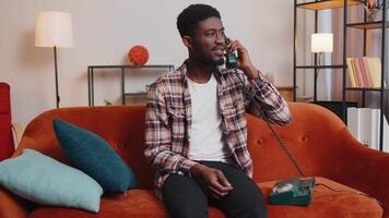 Young adult african american man enjoying talking on retro phone conversation with friends at home video