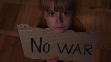 Afraid homeless toddler girl sitting holding inscription No War, hiding from bombing attack at home video
