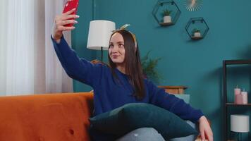 Woman on sofa at home with smartphone taking selfie on mobile phone cam, virtual call online. video