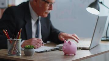 Piggy bank, senior business man accountant typing on laptop computer calculating money income. video