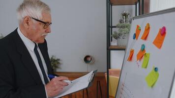 Senior business man making notes on board with stickers analyzing infographics use laptop computer. video