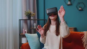 Young girl using virtual reality headset glasses at home play 3D game making gestures with hands video