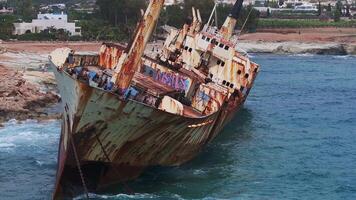 Aerial footage of the Edro III shipwreck in Cyprus, showing its rusted hull with graffiti, turquoise waters, and nearby coastal settlement with palm trees. video