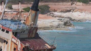 Aerial view of the Edro III Shipwreck in turquoise waters near a rocky shoreline in Cyprus. Gentle waves and visitors walking along the coast are visible. video