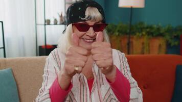 Grandmother old woman looking at camera raises thumbs up agrees with something positive good at home. video