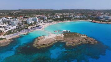 Aerial view of Ayia Napa, Cyprus, showing Nissi Beach, turquoise waters, boats in motion, beachfront resorts, and lush greenery in the backdrop. video