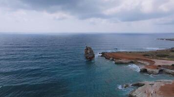 Aerial view of the Edro III Shipwreck near Cyprus' rocky shoreline, with turquoise waters, rugged terrain, homes, and open fields in motion. video