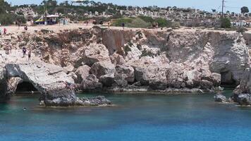 Limestone cliffs and sea caves of Ayia Napa, Cyprus, with turquoise waters gently moving. A small settlement and tourist activity are visible. video