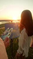 A young teacher is teaching a student how to draw landscapes from nature, in a field, in the rays of the setting sun. Vertical. video