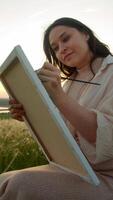 Left-handed artist, seated, meticulously applies paint with a paintbrush to canvas, utilizing gouache, in the fading light of the setting sun. Portrait. video