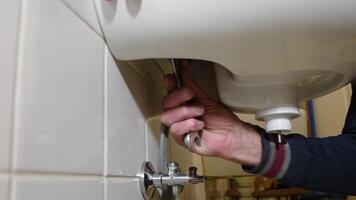 owner hung a new white ceramic sink on the tiled wall in the bathroom by himself and tightens the nuts with a wrench, plumbing concept, video