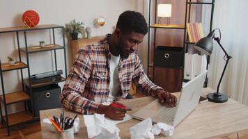 Tired man at home office falling asleep on table with laptop computer, crumpled sheets of paper. video
