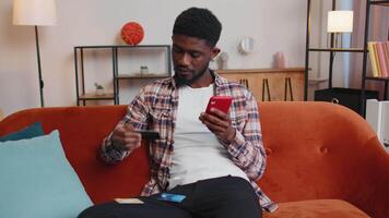 Man sitting at home using credit bank card and smartphone while transferring money online shopping. video