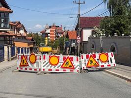 Street closed for construction work. Traffic barriers with warning signs and excavator visible in residential area. photo