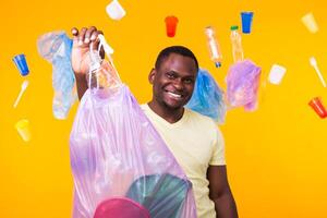 Problem of trash, plastic recycling, pollution and environmental concept - happy african american man carrying garbage for recycling on yellow. photo