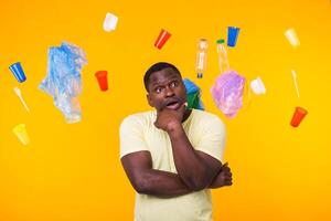 Problem of trash, plastic recycling, pollution and environmental concept - Surprised african american man looking on trash on yellow background. He is thinking about ecology photo