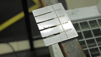 Weld gauge measuring bead size on metal. Close-up of a welding gauge tool used to measure bead width on a rusty steel bar during quality control inspection video
