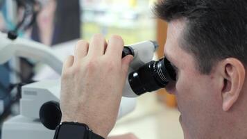 Man using microscope for close examination. Close-up of a man looking through a binocular microscope, adjusting focus during a detailed observation in a video