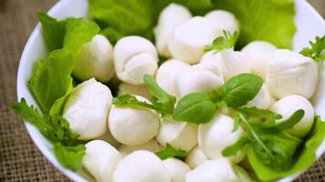 mini mozzarella in white bowl with greens on grey background. Top view video