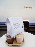 Pasir Mas Malaysia-2, June,2024. Cold beverage in a branded plastic cup with a carton holder and paper bag featuring the slogan's Necessity not a Luxury. Food and beverage franchise company. photo