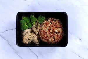 a black container with rice, broccoli and chicken photo