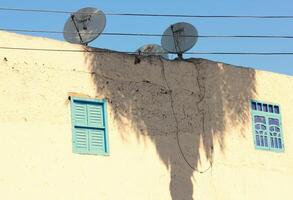 Wall of an old house with palm trees shadow and satellite dishes on rooftop. photo