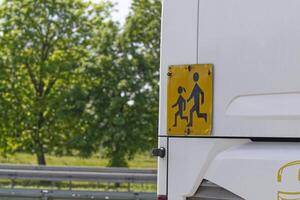 A yellow and black sign at the rear of the school bus warns of running students photo