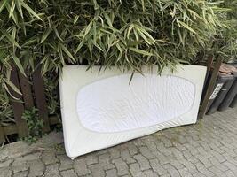 A mattress with fitted sheets was temporarily stored outside for disposal photo