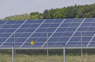 A Northern German solar farm, a field full of solar panels is protected by a fence with a warning sign photo