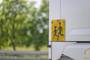 Yellow and black sign at the rear of the school bus warns of running students photo