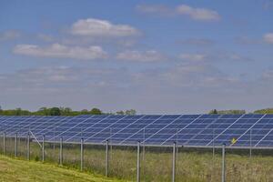 A Northern German solar farm is a field full of solar panels is protected by a fence with a warning sign photo