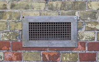 A rusty metal grid is built into a wall, which has a wide steel frame photo