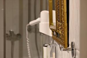 Hotel bathroom with white hairdryer next to a mirror with a beautiful golden frame in Baroque style photo