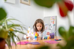 Little girl painting ceramic figurine with colorful paints at table photo