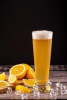 Glass of cold wheat beer with foam beside fresh lemon wedges and ice cubes on wooden surface. Concept citrus craft beer, summer refreshment and flavor pairing. Cold wheat beer with lemon and ice cubes photo