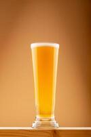 Cold beer with foam served in tall clear glass on wooden surface against warm gradient background. Concept beer clarity, classic lager and refreshing beverage. Cold beer in tall clear glass with foam photo