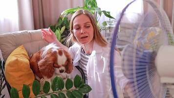 A woman and her dog enjoy the cool air from a fan in their home on a hot day. It helps her cope with the stuffiness and restore her strength. Relaxation concept, wellness centers. video