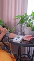 An old woman measures her blood pressure with a tonometer in her cozy apartment. This action helps to monitor hypertension and heart problems. The concept of medical devices. video