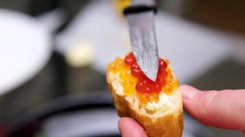 Spreads red caviar on bread with knife. Chef smears salmon caviar on toast. Close-up of knife is spreading caviar on bread. Tasting salmon caviar salted roe, black background slow motion video