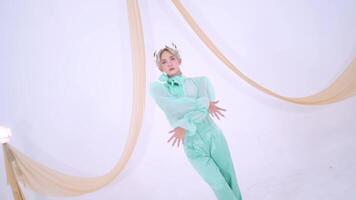 A stylish individual poses in a mint green outfit against a minimalist white backdrop. Soft drapes of fabric add a touch of elegance to the scene. video