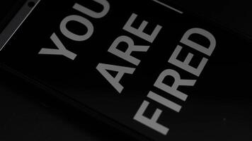 Close-up of smartphone screen displaying stark 'You Are Fired' message in a dimly lit environment video