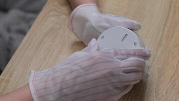 Hands in Protective Gloves Carefully Closing the Lid on a Smoke Detector on Wooden Surface at Home video