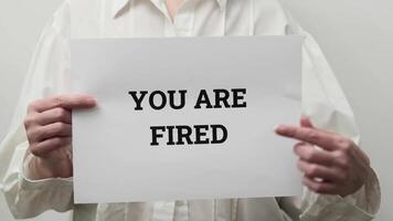 Person Holding a Sign with Bold 'You Are Fired' Message in a Neutral Background Setting video