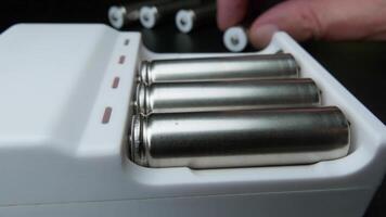Close-up of Metallic AA Batteries Being Placed in a White Portable Charger Device on Black Background video
