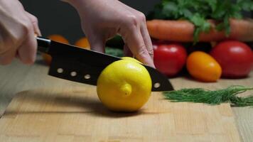 Close-up of Hand Slicing Fresh Lemon on Wooden Cutting Board with Colorful Vegetables in Kitchen video
