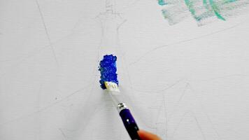Brush painting blue acrylic on canvas sketch. Close-up of an artist applying vibrant blue paint with a brush on a lightly sketched canvas during the early stage video