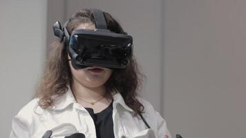 Woman using virtual reality headset indoors. Young woman wearing a high-tech VR headset and holding controllers, immersed in a virtual experience in a modern video