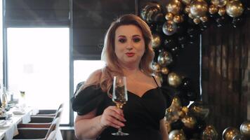 Woman turning with wine glass at celebration. Elegant woman in black dress turns playfully while holding a wine glass at a festive event with balloon video